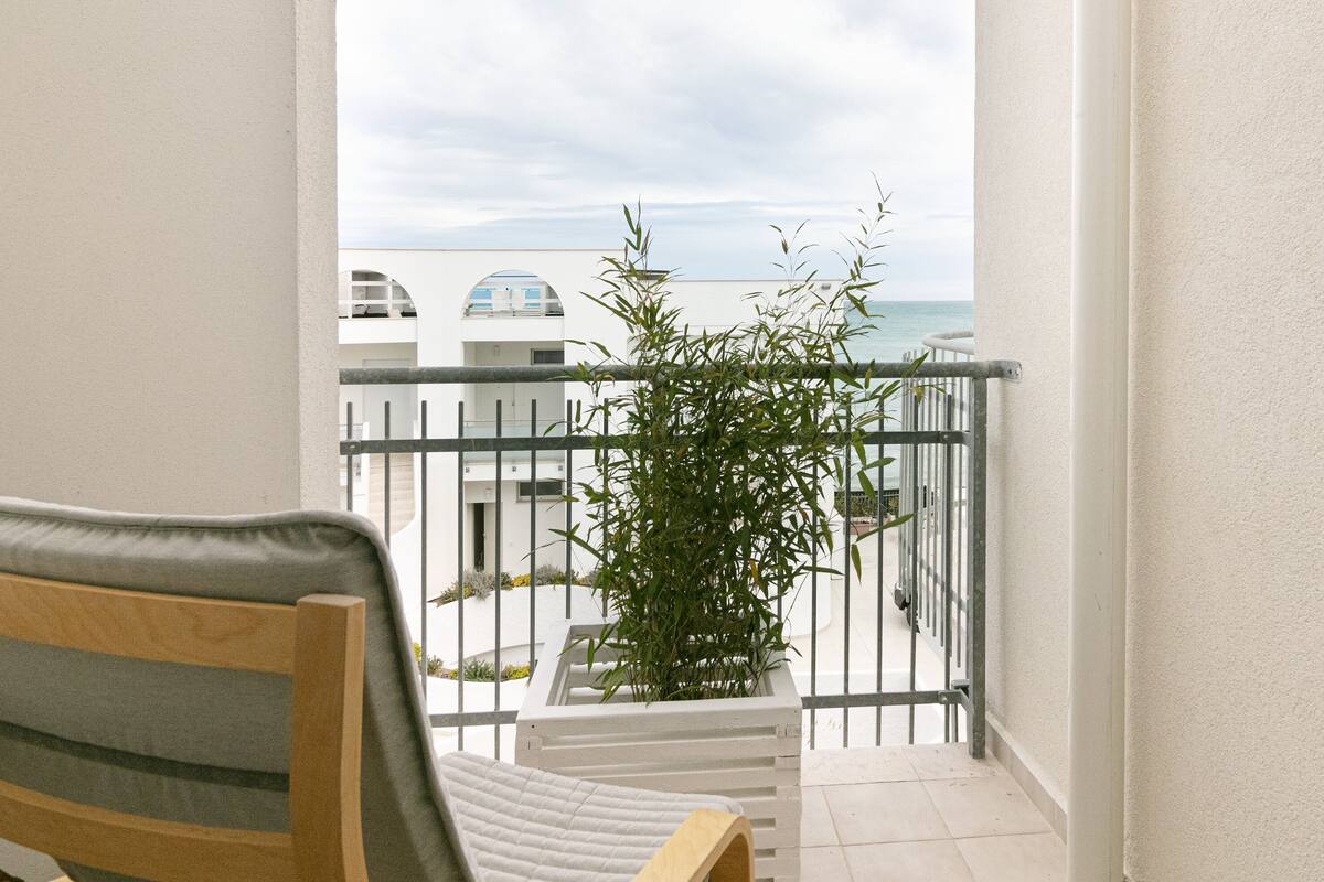 A balcony with a view of the sea, a chair, and a potted plant.