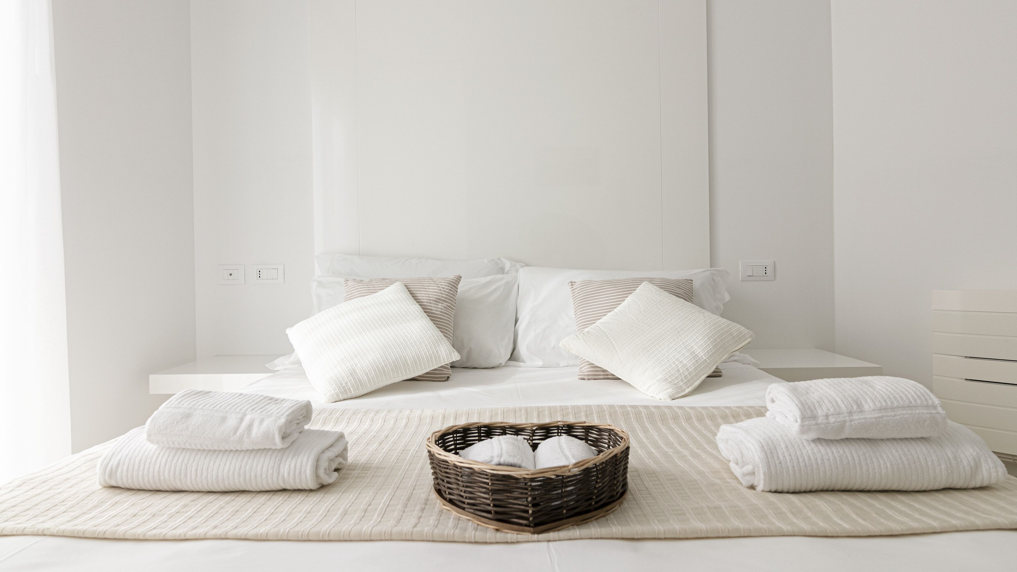 Une chambre à coucher au style minimaliste, avec un lit, des oreillers et un panier rempli de serviettes.