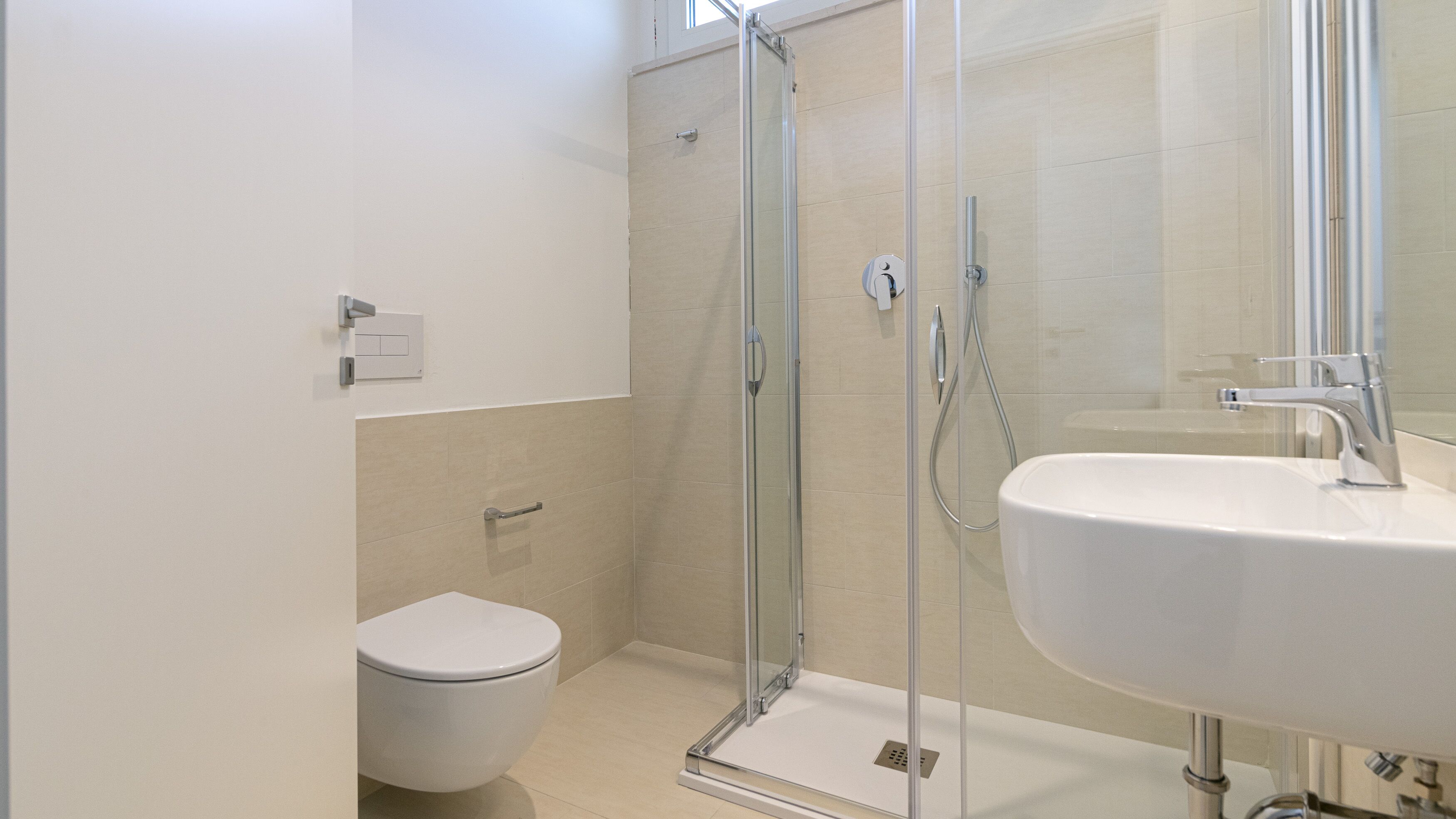 Un baño moderno con ducha envuelta en vidrio, un lavamanos blanco y un inodoro.