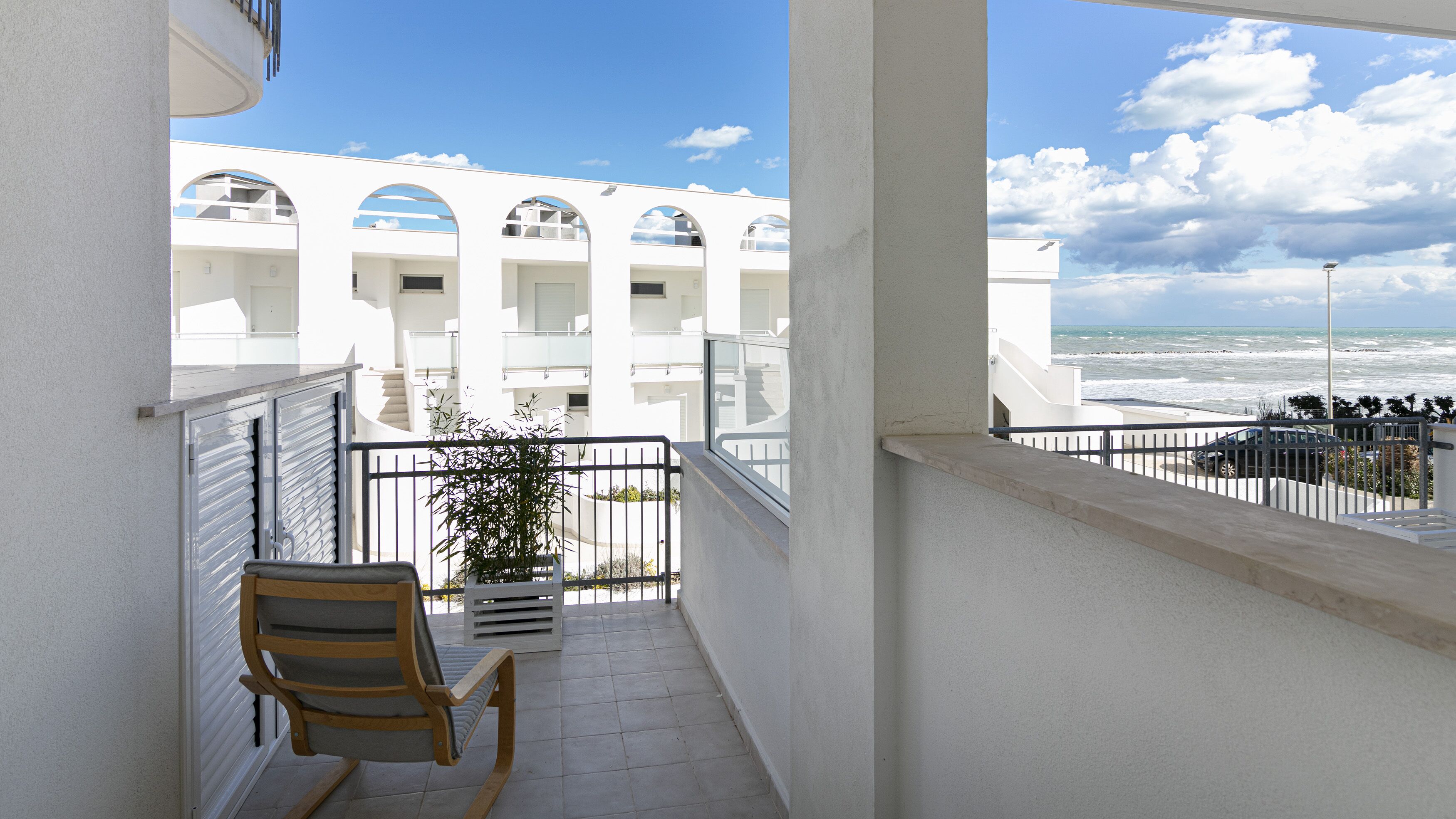 A balcony with a view of a white building with arched windows and a beach.