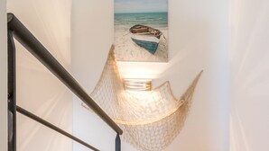Una escala amb una obra d'art penjada a la paret que representa una escena de platja, una cadira l'hamaca i una làmpada.