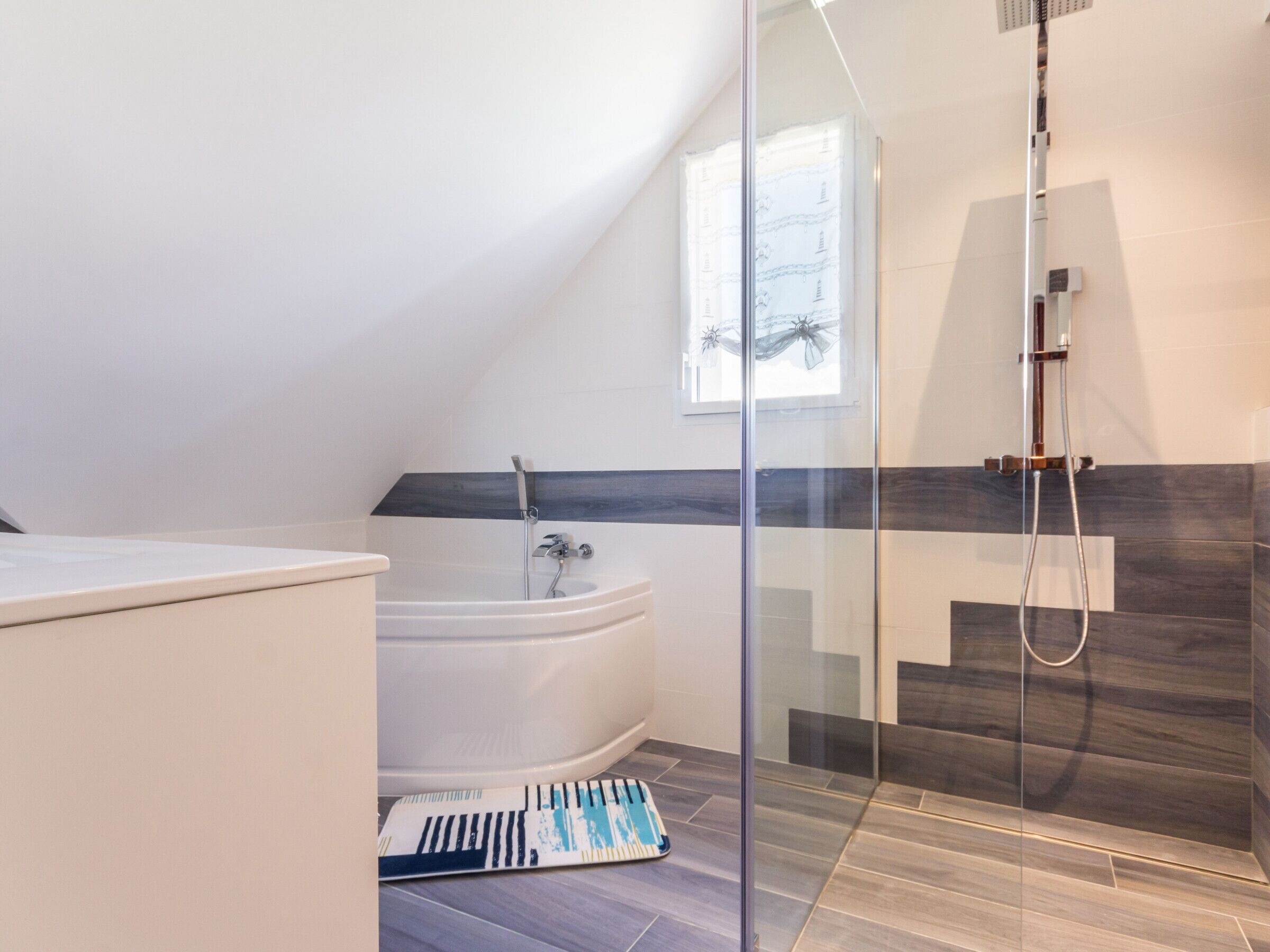 Une salle de bain moderne avec une baignoire sur pieds, une douche à parois de verre et une fenêtre laissant entrer la lumière naturelle.