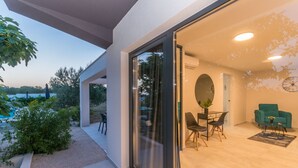 A modern interior with a dining area, a sofa, and a large window overlooking a garden. - Modern villa BlackWood in Crno, secluded area, near Zadar center, near the beach, private pool, en suite bathrooms (Crno)