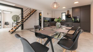 A modern kitchen with dark cabinets, a built-in oven, and a dining area with a glass table and black chairs. - Modern villa BlackWood in Crno, secluded area, near Zadar center, near the beach, private pool, en suite bathrooms (Crno)