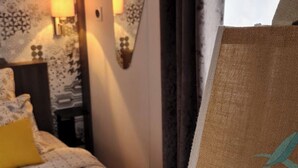 Ett hotellrum med ett mönstrat överkast på sängen, en spegel, ett nattduksbord med en lampa och en handduk på sängen.