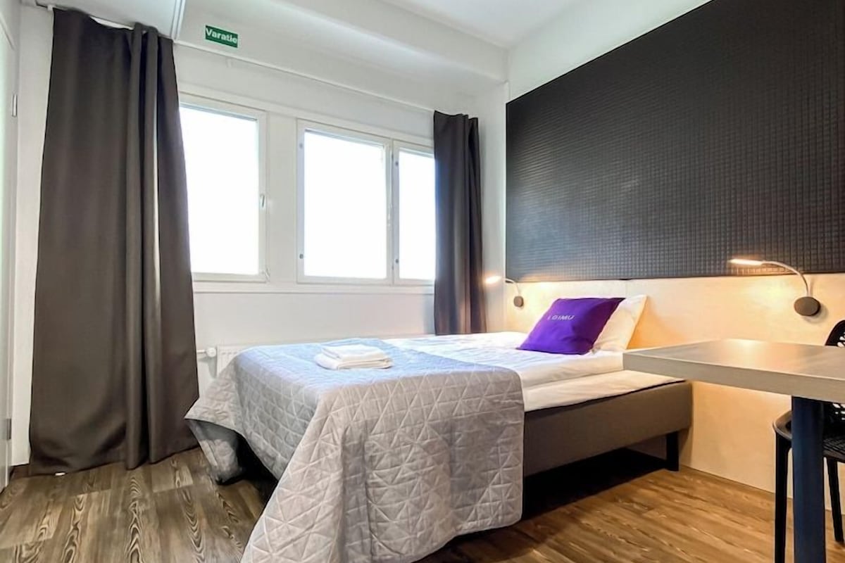 A hotel room with a bed, a desk, and a window.
