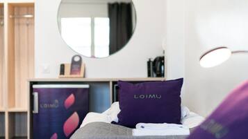 A hotel room with a bed, a round mirror, a nightstand, and a wall-mounted light fixture.