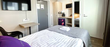 Habitación de hotel con cama, escritorio, televisor montado en la pared y armario.