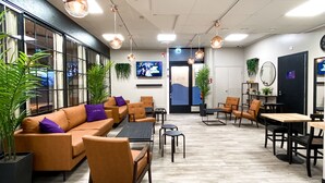 A modern lounge area with a sofa set, tables, and chairs, large windows, and ceiling lights. - Hotelli Loimu (Raisio)