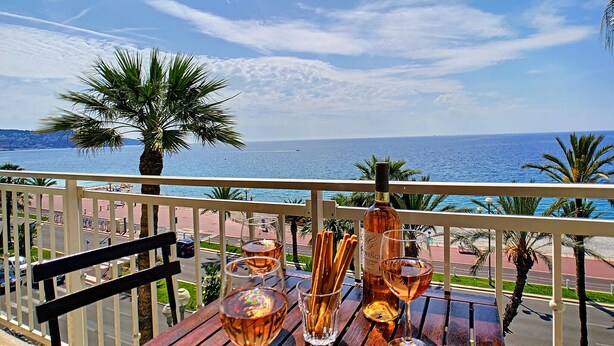 Une table en bois, une bouteille de vin, deux verres et un verre de vin, le tout sur un balcon donnant sur la mer.