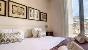 Une chambre d’hôtel avec un lit, des oreillers, une table de chevet, une fenêtre donnant sur un paysage agréable et des tableaux encadrés au mur.
