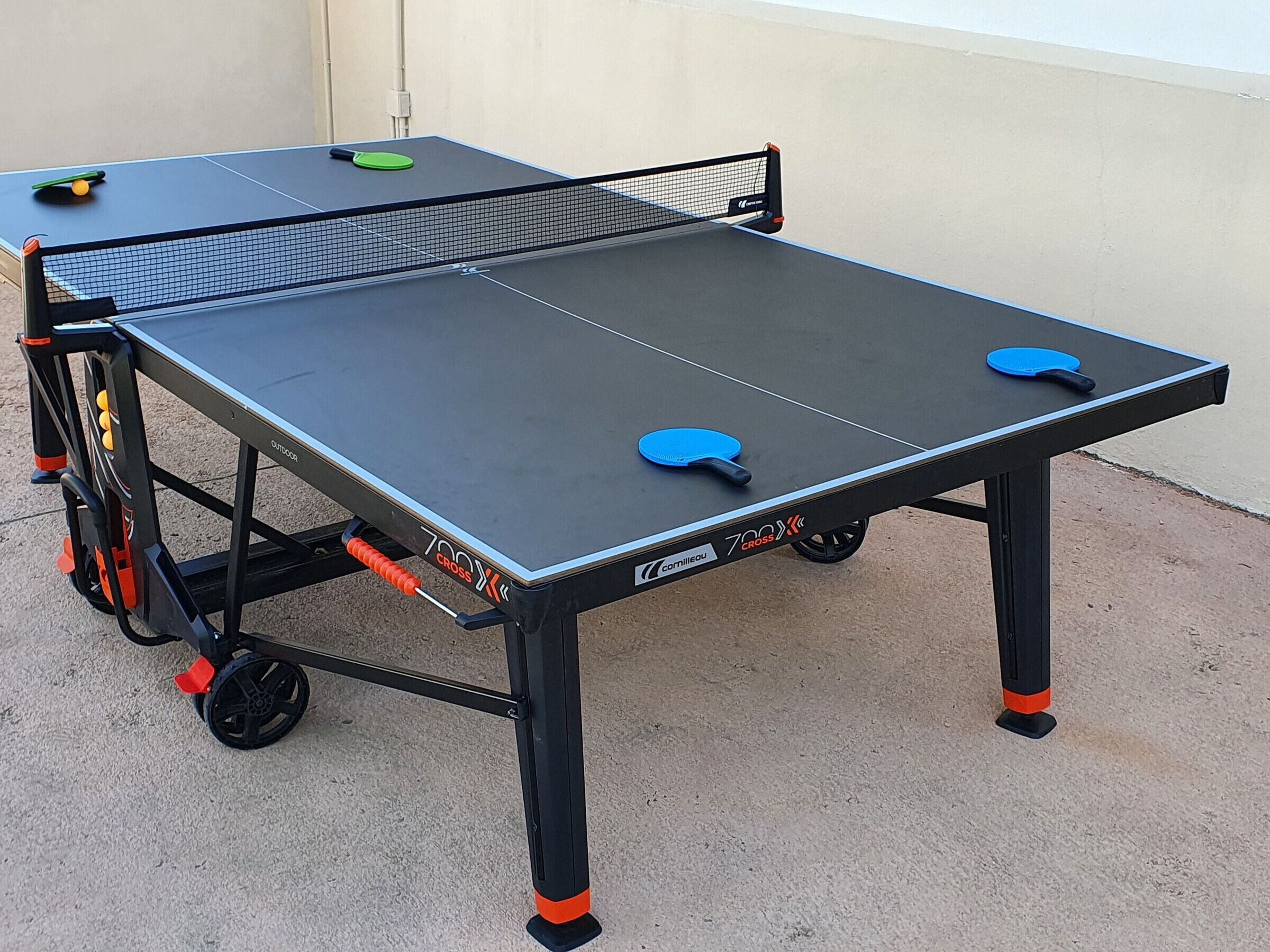 A portable ping pong table with wheels, a net, and two paddles.