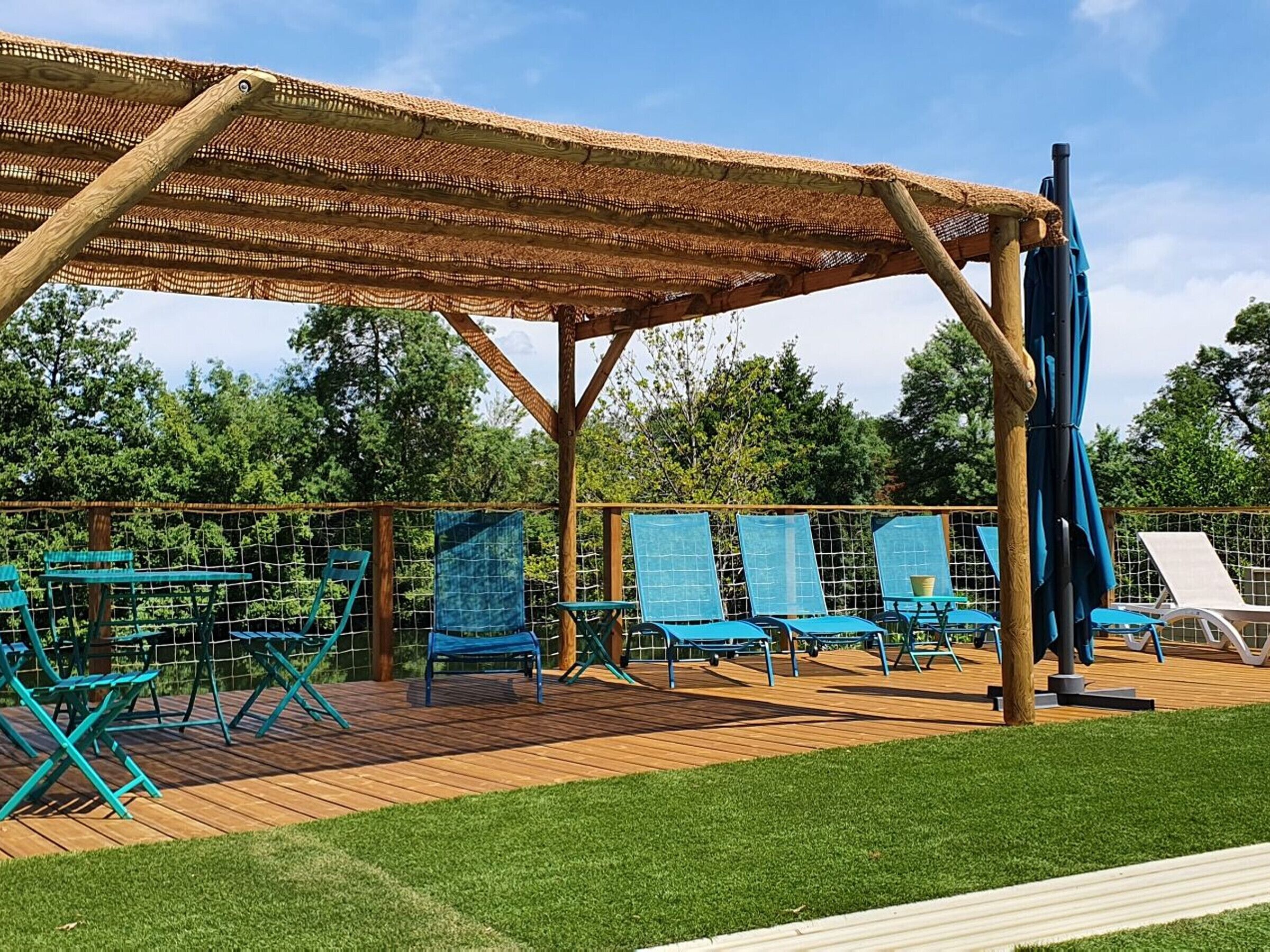 A covered outdoor area with wooden deck, blue lounge chairs, and a thatched roof structure.
