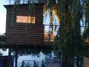 A wooden cabin with a balcony and a window, surrounded by trees and a body of water. - Family Retreat with Private Pool and River Views near Zoo (La Flèche)
