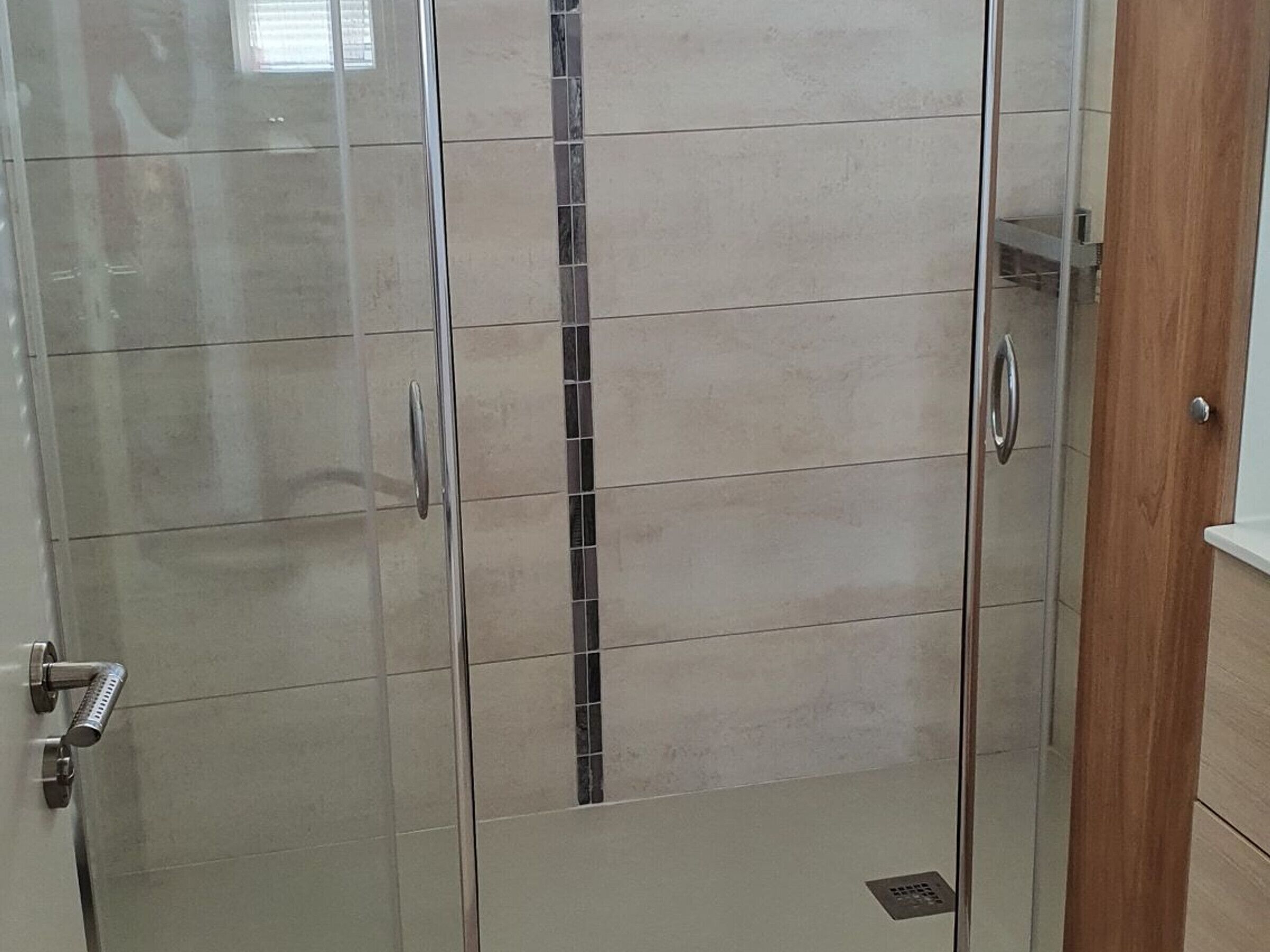 A bathroom with a glass shower enclosure, a wooden door, and a tiled floor.