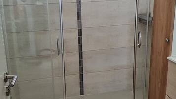 A bathroom with a glass shower enclosure, a wooden door, and a tiled floor.