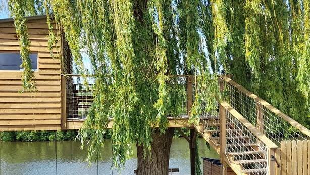 Een houten terras met een trap naar een houten gebouw, met uitzicht op een waterlichaam.