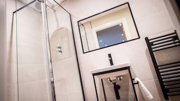 A modern bathroom with a glass shower enclosure, a sink with a black countertop, and a towel rack.