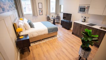 Una habitación de hotel moderna con una cama, mesita de noche, lámpara y una pequeña zona de comedor con sillas.