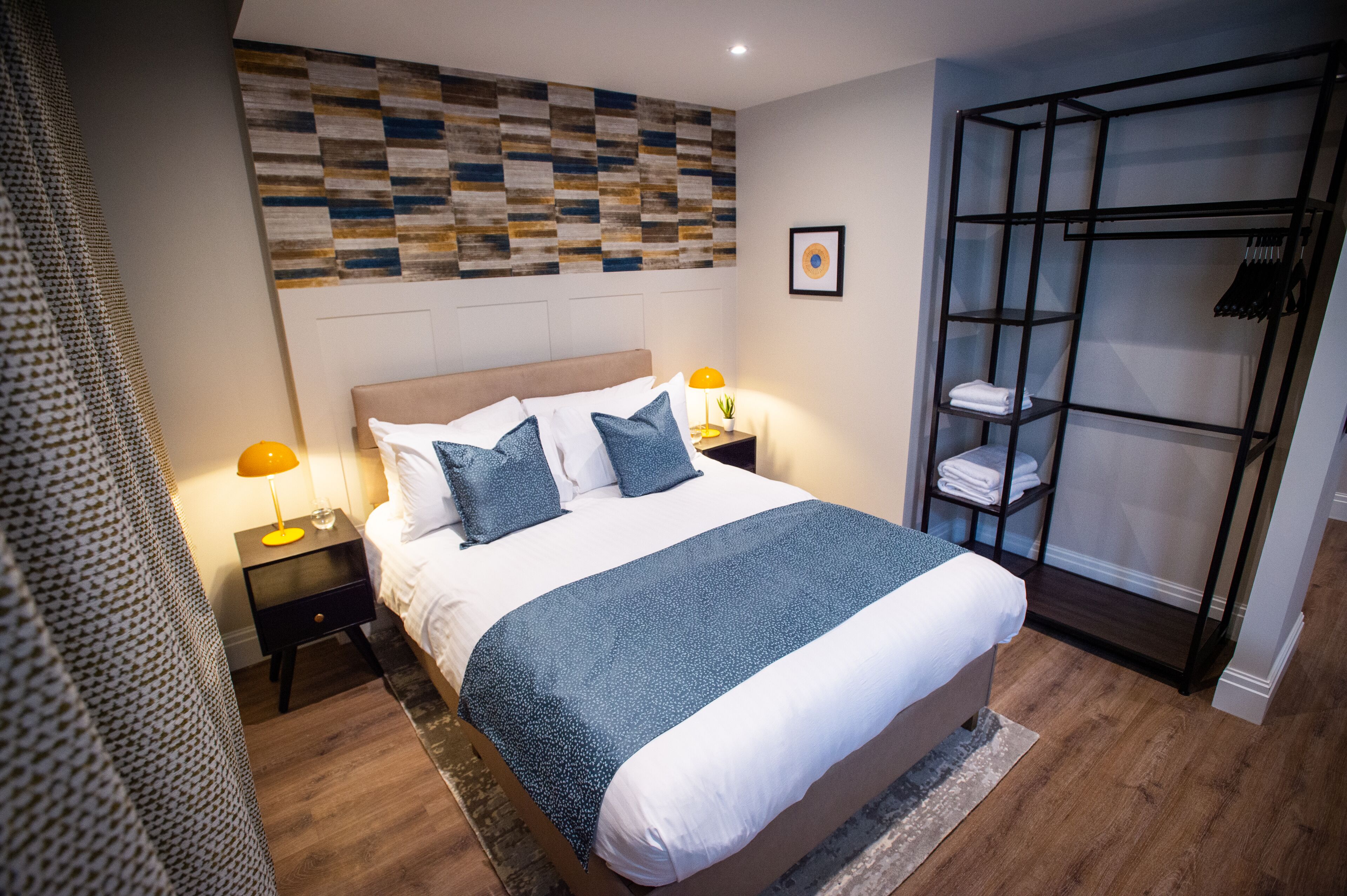 A neatly arranged bedroom with a bed, bedside lamps, a wall art piece, and a built-in wardrobe.