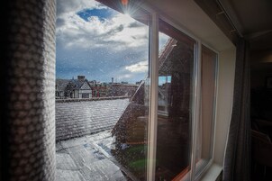 A view through a window with raindrops, a brick roof, and a building with a sloped roof in the background.