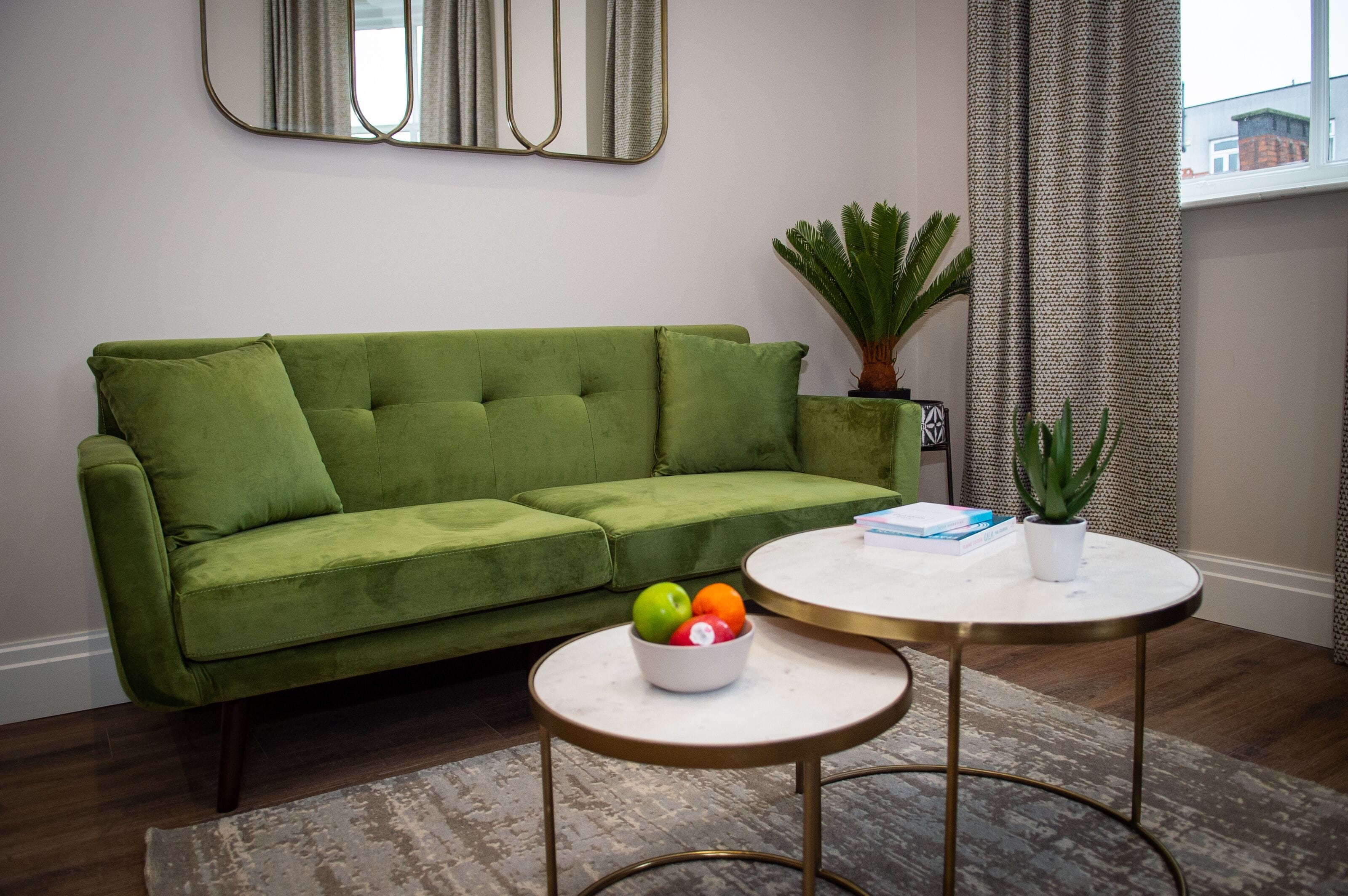 Een groene bank, een klein rond tafeltje met een schaal fruit en een potplant.