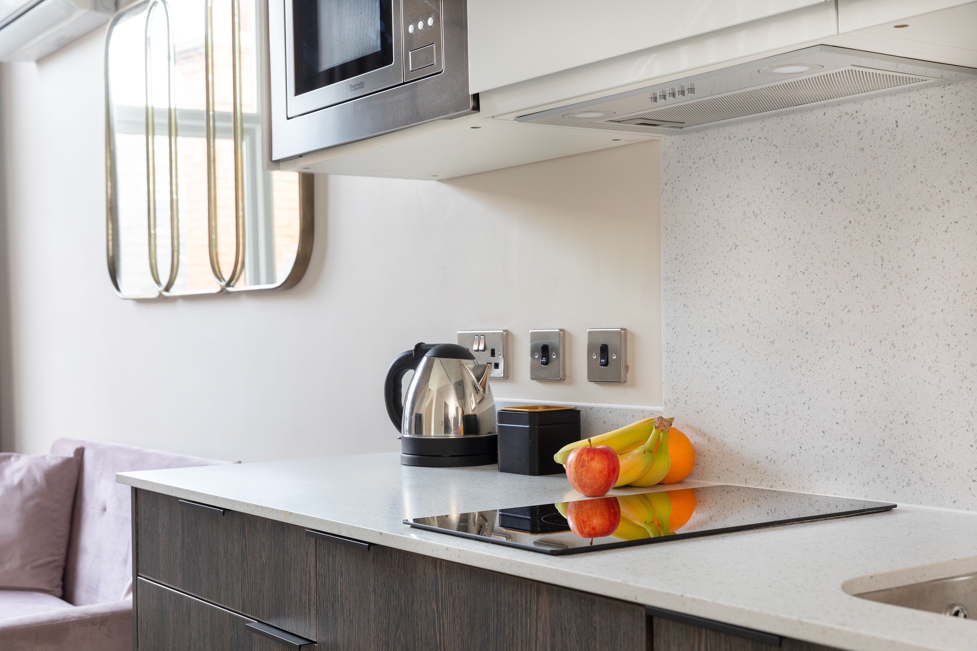 A modern kitchen with a microwave, kettle, and a tablet on the counter.