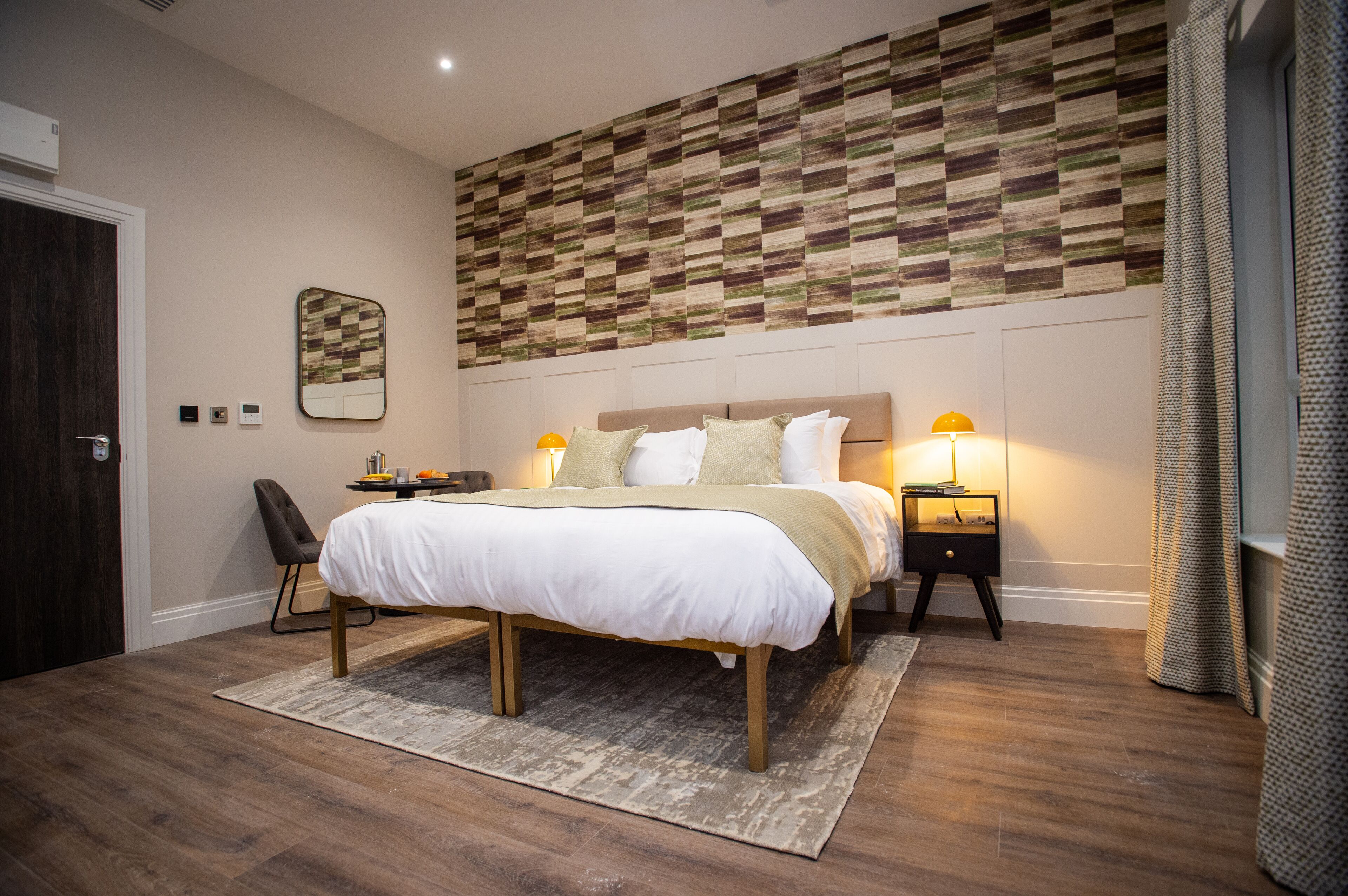 Ein modernes Schlafzimmer mit einem großen Bett, Nachttischlampen, einer Wanddekoration und Holzboden.