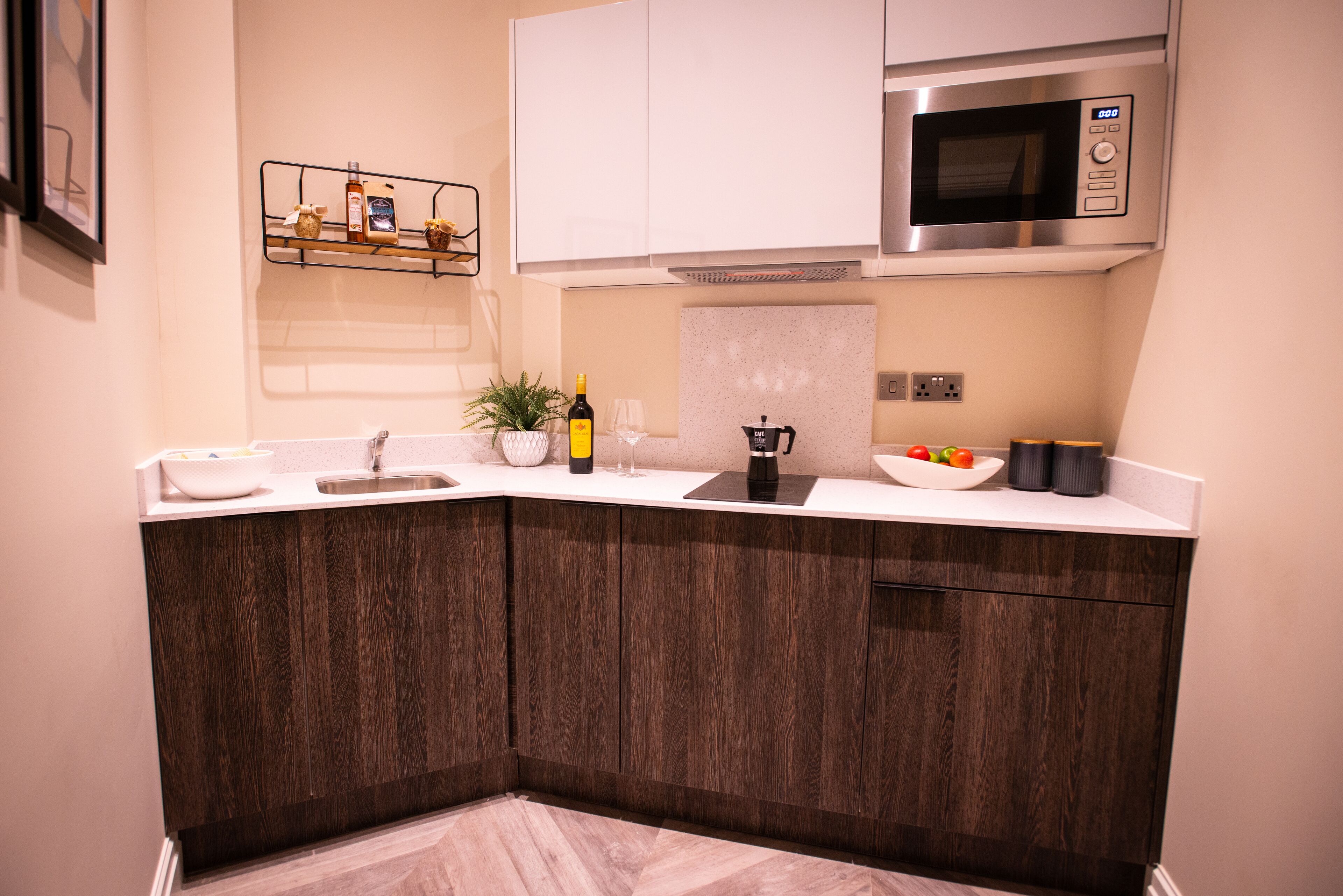 A modern kitchen with dark wood cabinets, white countertops, a built-in microwave, and a wine bottle on the counter.