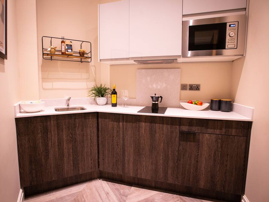 A modern kitchen with dark wood cabinets, white countertops, a built-in microwave, and a wine bottle on the counter.