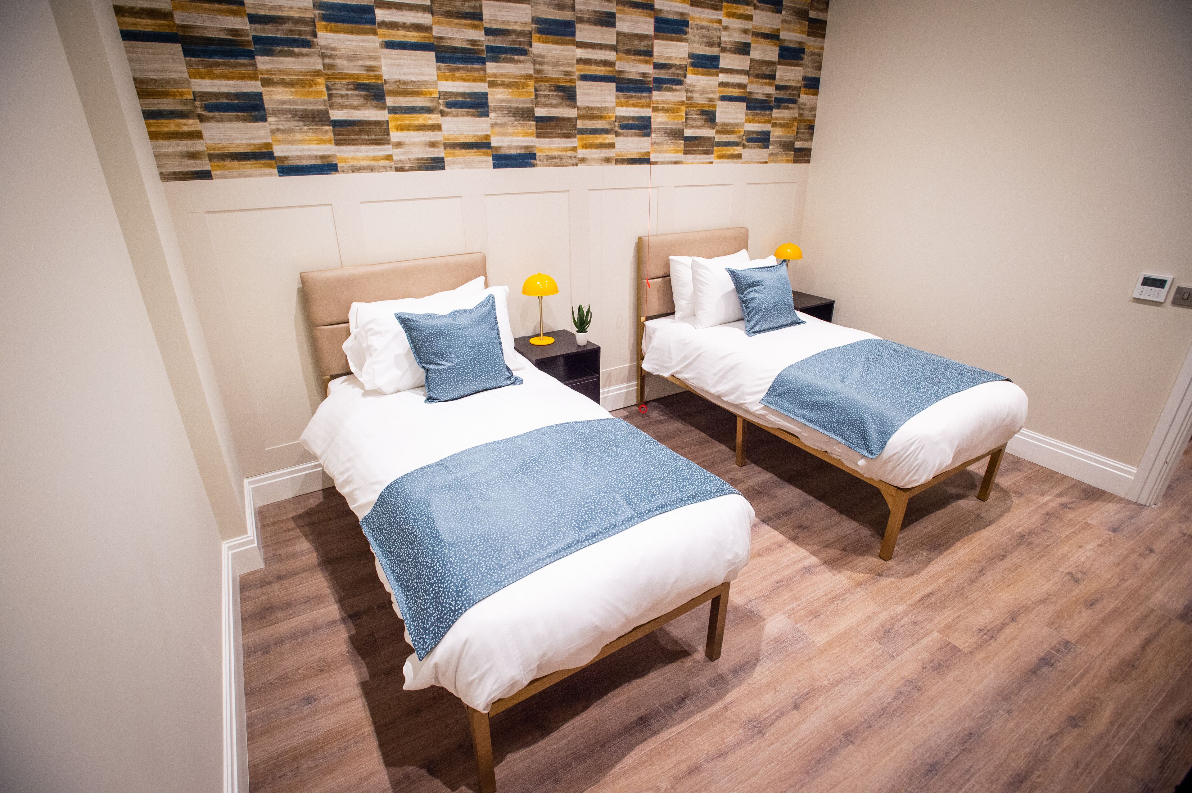 Une chambre d’hôtel avec deux lits, un plancher en bois, un mur décoratif et une petite table de chevet avec une lampe.