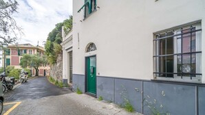 Une rue étroite bordée d’un immeuble blanc, avec une porte verte et des fenêtres dotées de barreaux en métal.