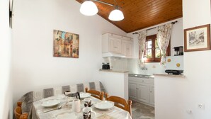Un comedor con una mesa preparada para cuatro, una cocina al fondo y un cuadro en la pared.