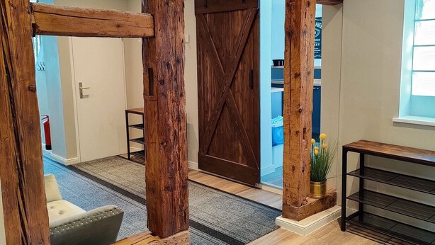 Una habitació àmplia amb sòl de fusta, una porta corredissa de biga i una petita planta sobre una console.