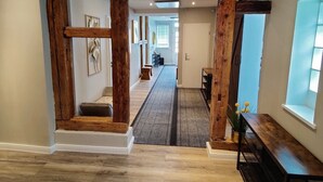 Un passadís ample amb bigues de fusta, un camí revestit de catifes i vista a una altra habitació.