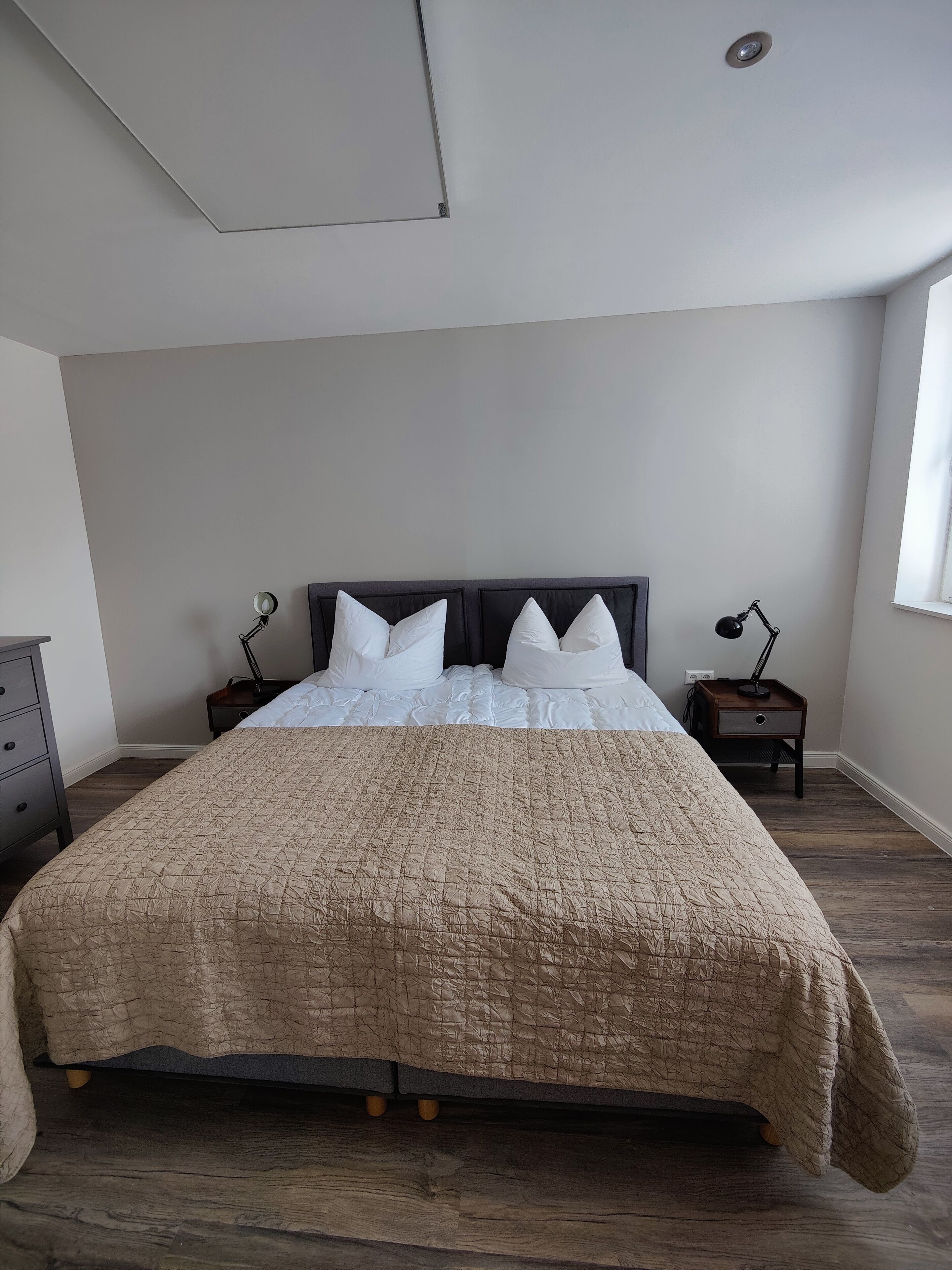 A bedroom with a large bed, two bedside tables, a nightstand, a dresser, and a window.