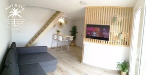 A modern living room with a grey sofa, a wooden TV stand, a staircase, and a dining area with a white table and chairs.
