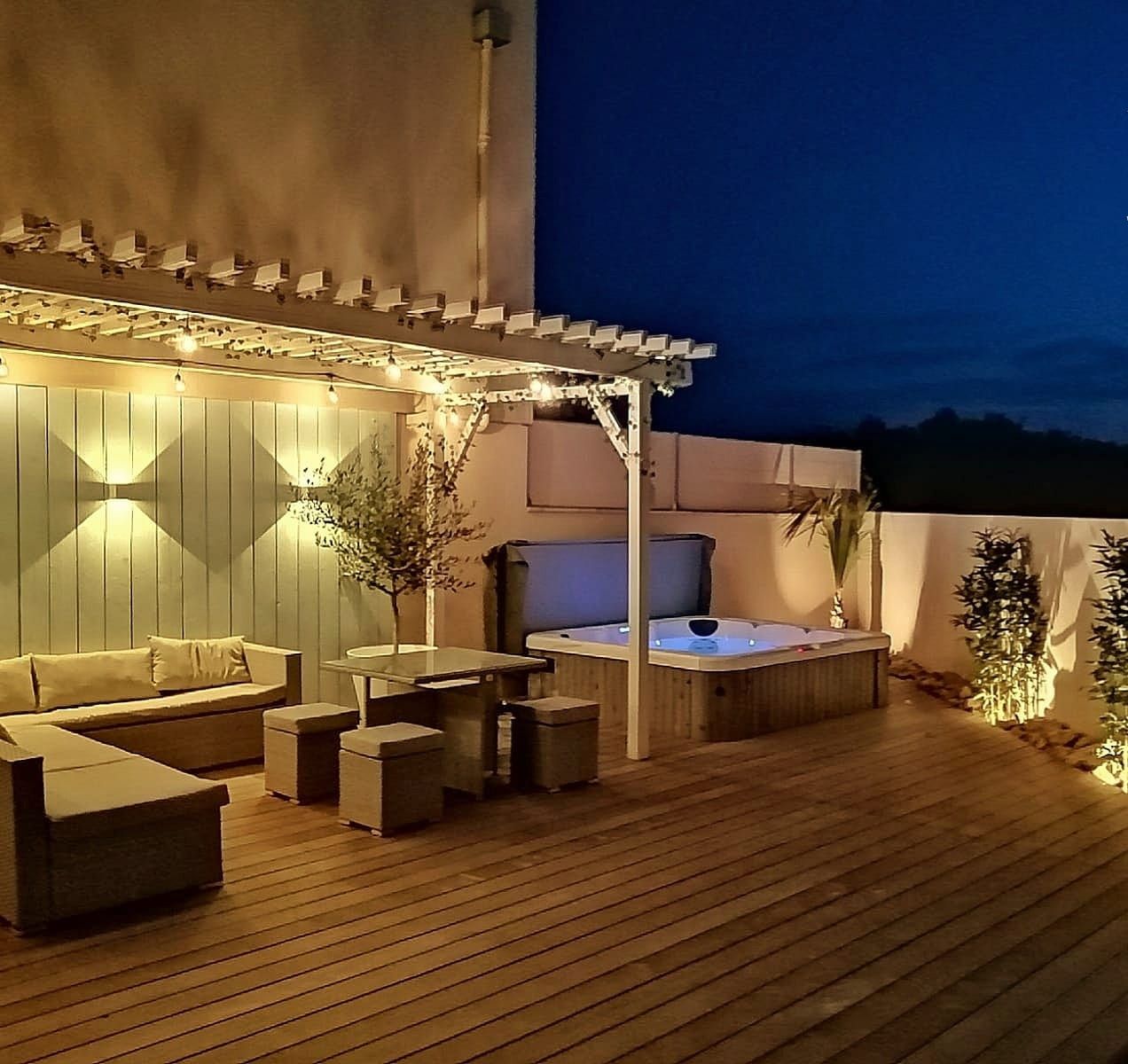 Een overdekt buitengebied met een jacuzzi, zitplaatsen en lichtslingers.