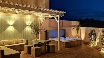 Een overdekt buitengebied met een jacuzzi, zitplaatsen en lichtslingers.