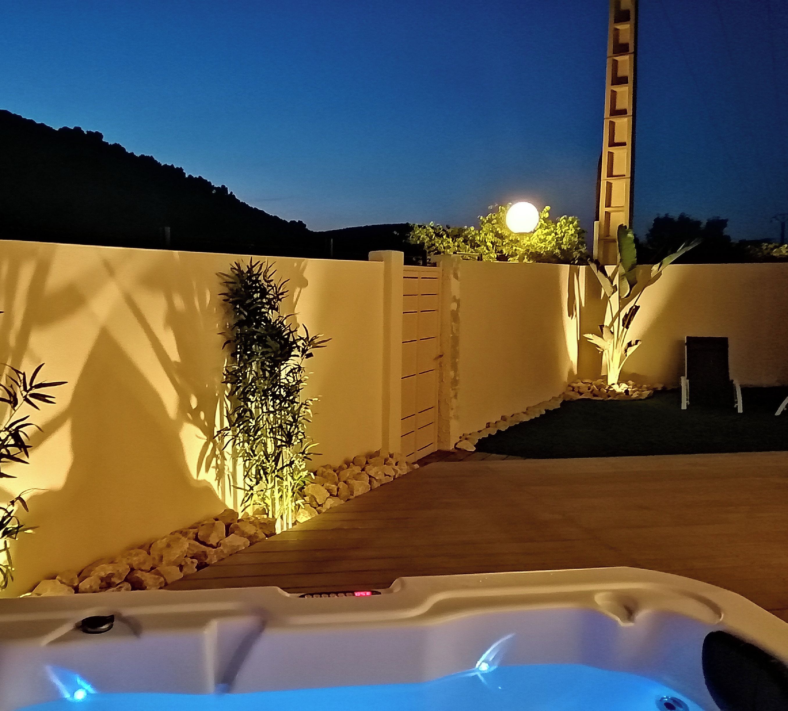A hot tub with a wooden deck, surrounded by a low wall with plants and a ladder.