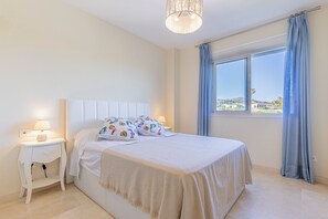 A bedroom with a bed, a nightstand, a lamp, a window with curtains, and a view of a landscape. - El Rinconcito (Rincon de la victoria)