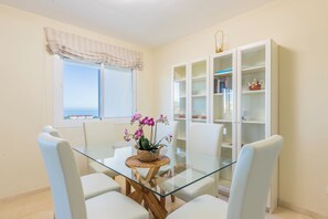 A dining area with a glass table and white chairs, a bookshelf, and a window with a view. - El Rinconcito (Rincon de la victoria)