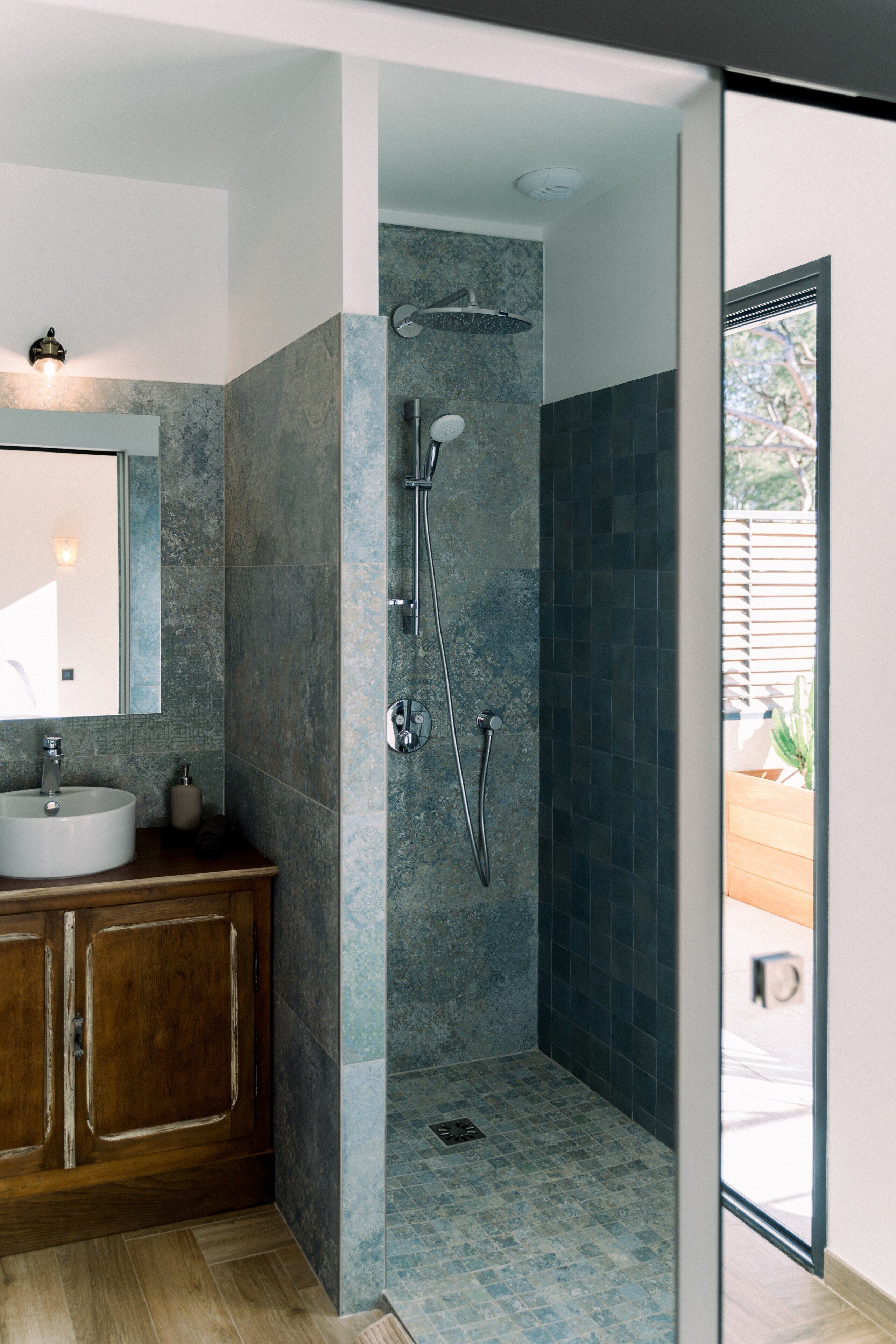 A modern bathroom with a freestanding sink, a mirror, a shower with a handheld showerhead, and a tiled floor.