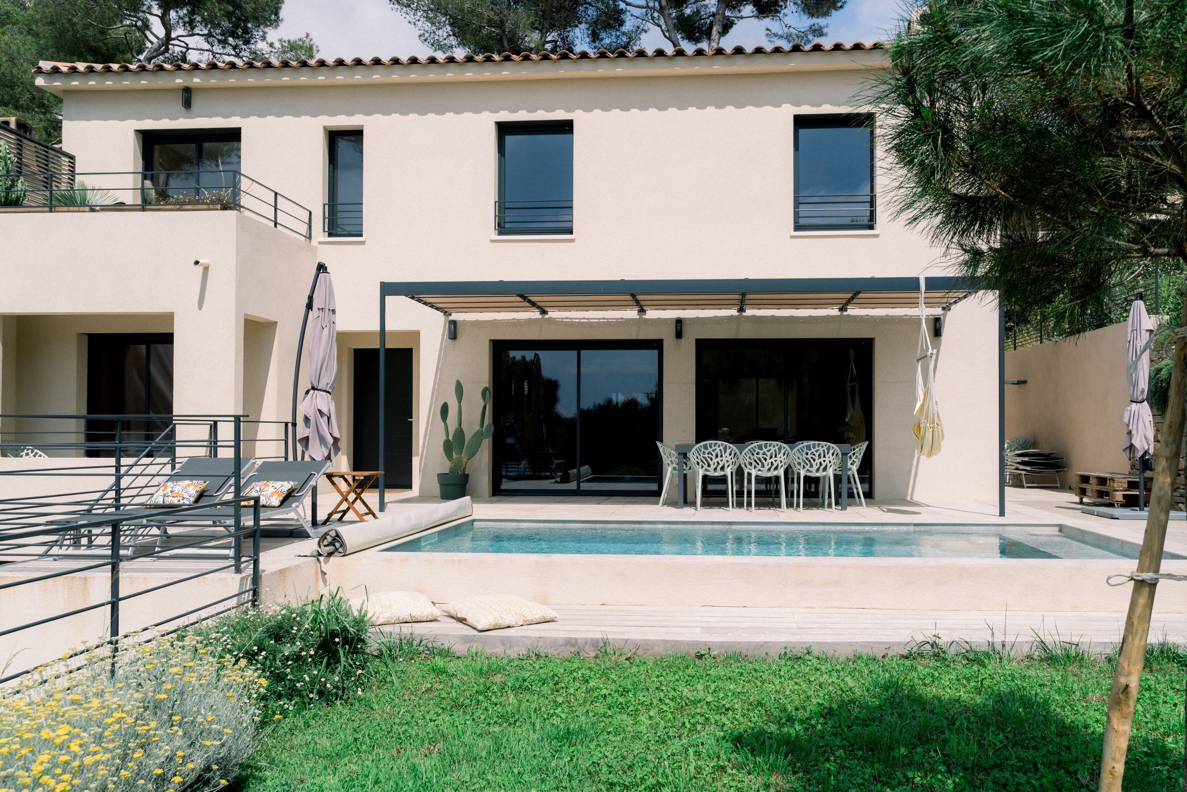 Ein zweistöckiges Haus mit Swimmingpool, Sitzgelegenheiten im Freien und einer überdachten Terrasse.