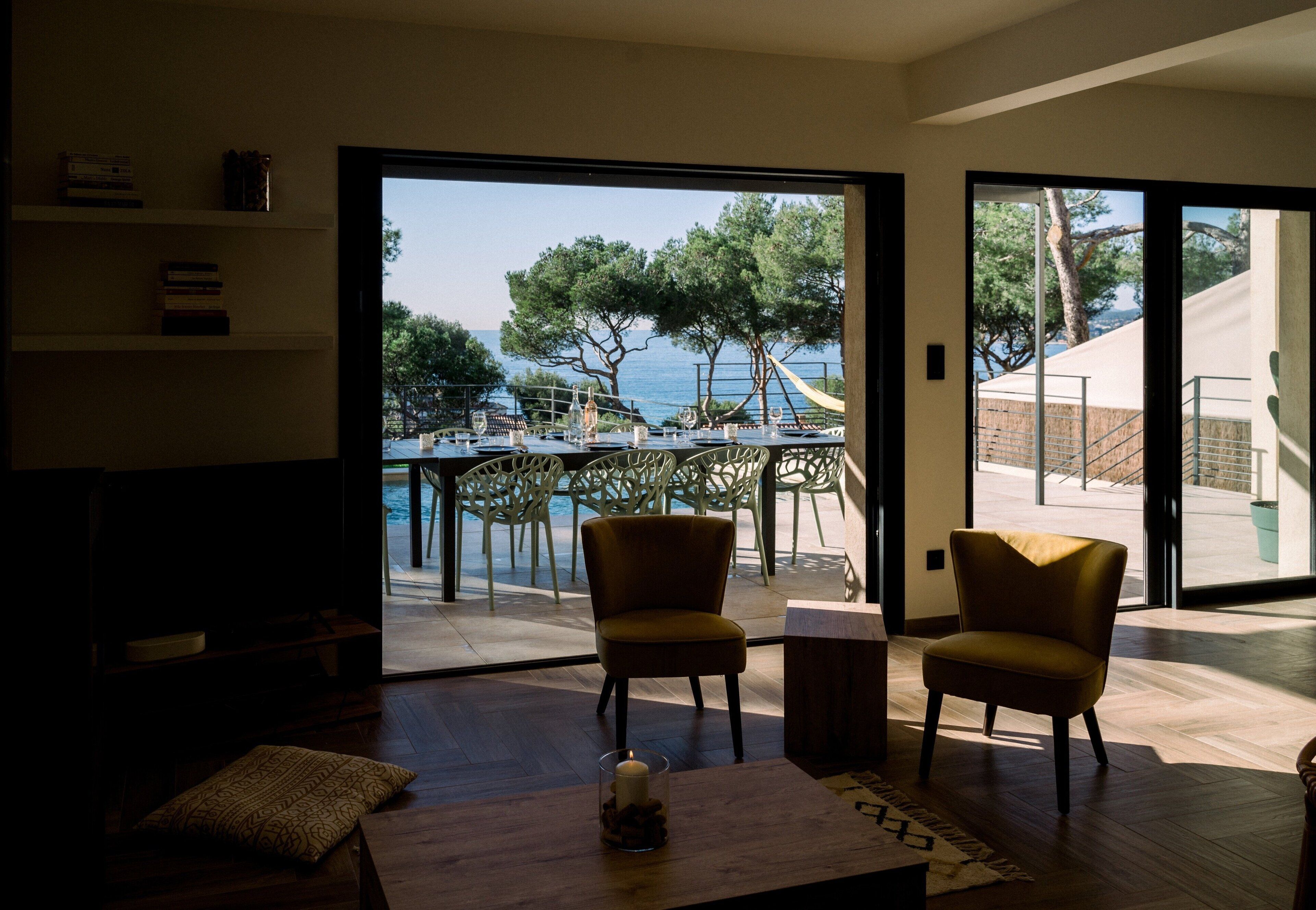Un salon moderne avec vue sur la mer, un coin repas avec des sièges extérieurs et un escalier menant à l’extérieur.