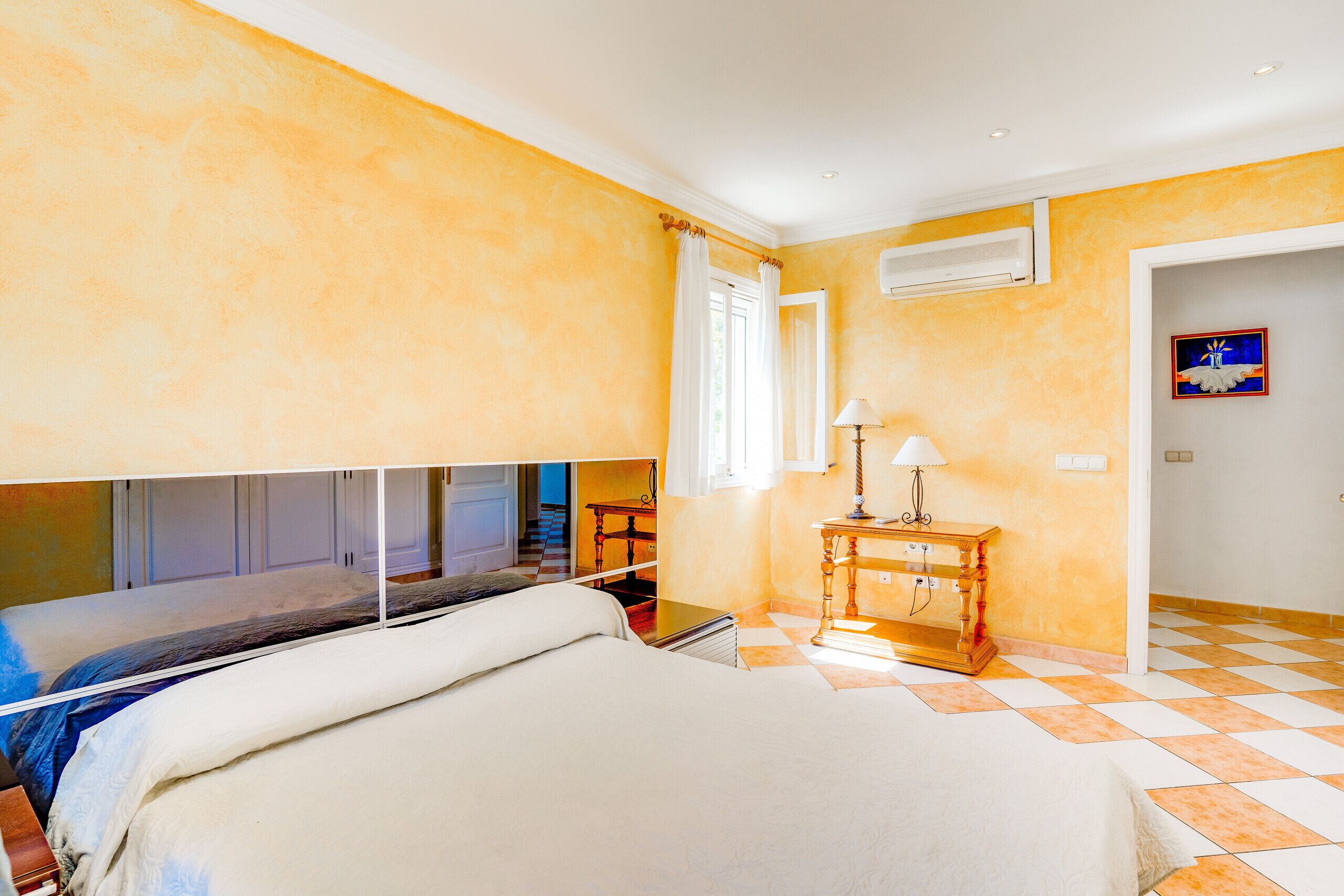 A hotel room with a bed, a wooden nightstand, a lamp, and a checkered floor.