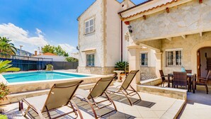Un espace piscine avec des chaises longues et un bâtiment en pierre doté d’un toit en tuiles.
