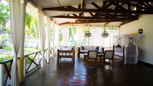 A covered outdoor area with a wooden bench, a sofa, and a chair. There is a bed with a canopy and a hanging light fixture. - Mambrui Villa (Malindi)