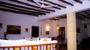 A room with a bed, wooden beams, a pillar with floral carvings, and wall-mounted artwork. - Mambrui Villa (Malindi)