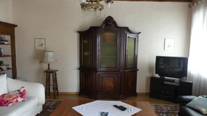 A living room with a wooden cabinet, a white sofa, a coffee table with a remote control, a television, and a chandelier. - Apartment in old rectory with lake view, terrace and garden - 3 persons (Ghiffa)